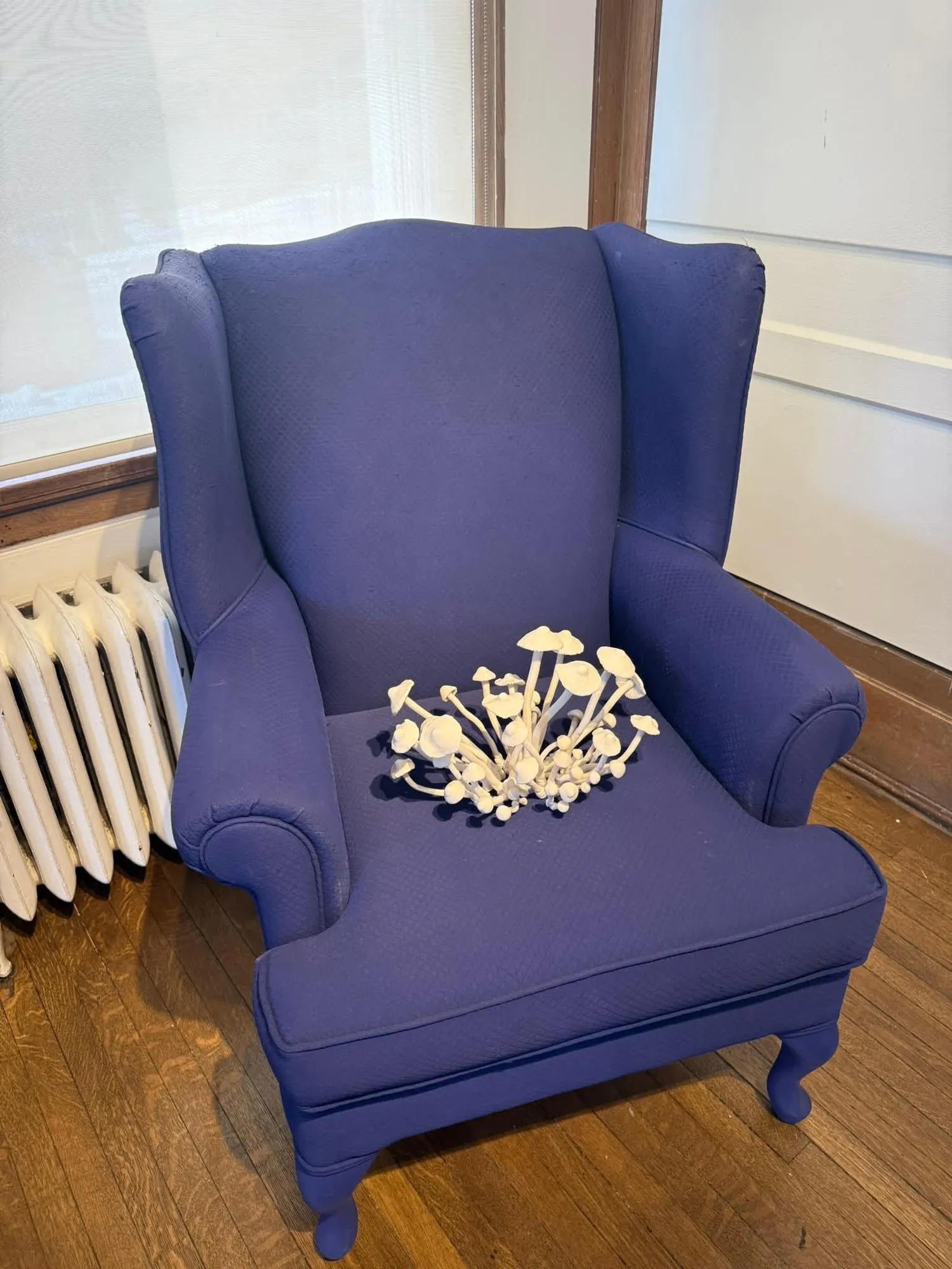 Blue wingback chair with a white ceramic mushroom cluster sculpture placed on the seat