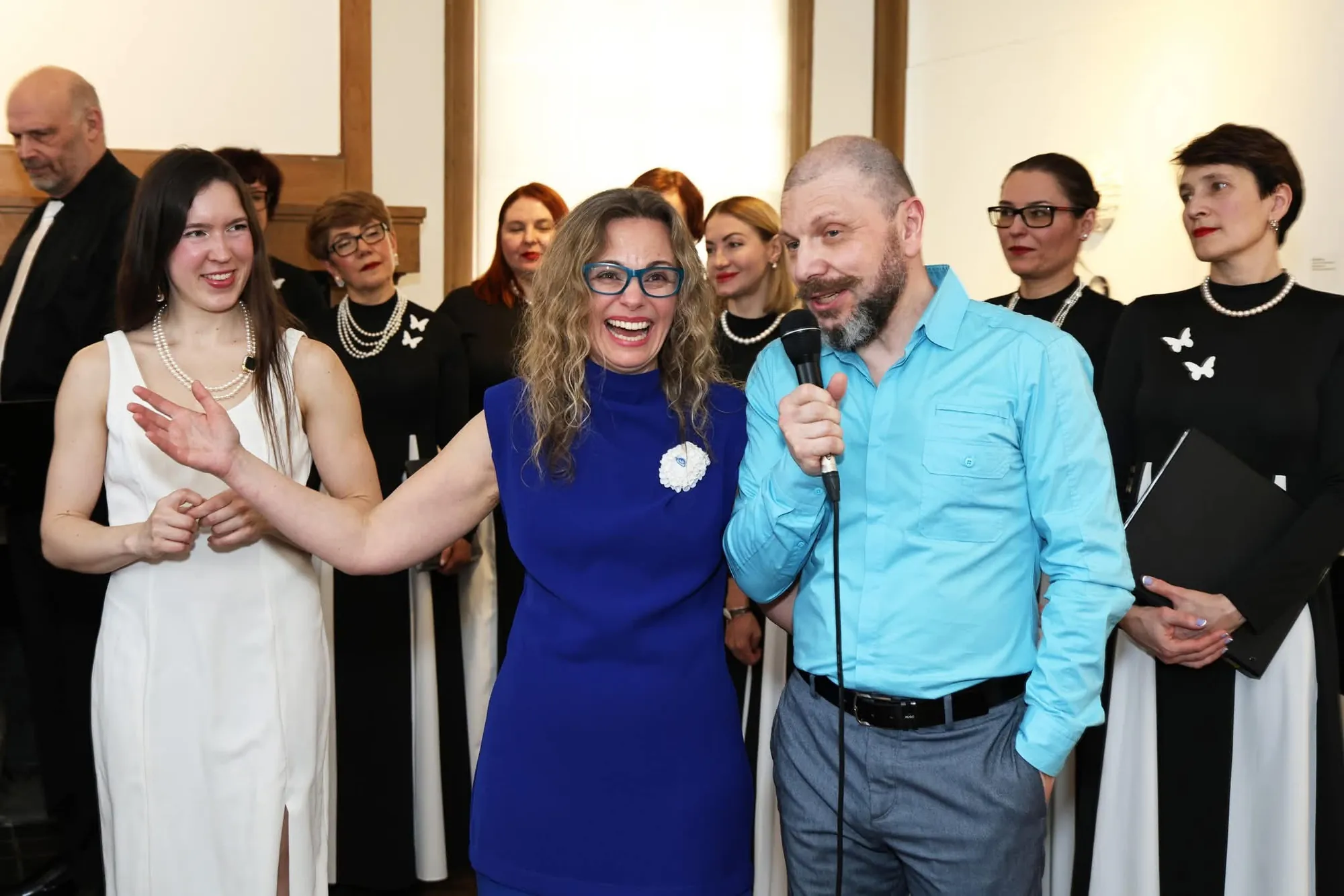 Opening reception with Tanya Besedina and a speaker at the microphone, AVE Choir members in black and white behind them