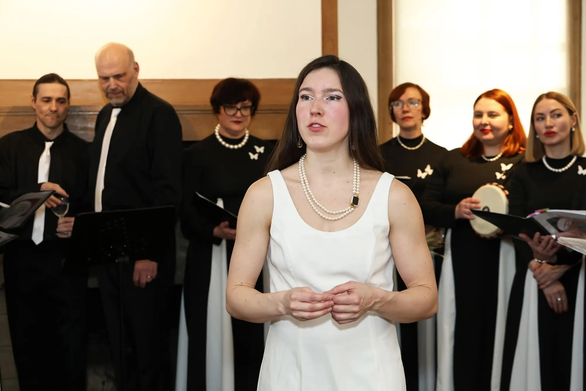 A soloist in a white dress performing with the AVE Choir in black and white behind her