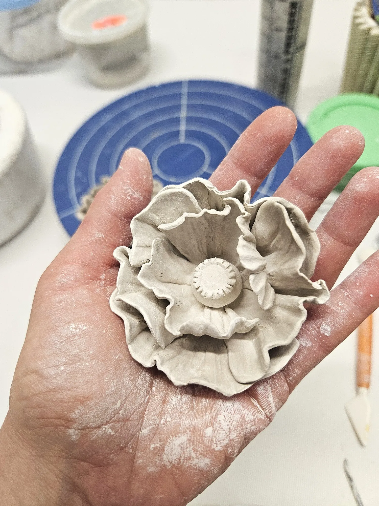 An unfired clay poppy held in the artist's hand, freshly shaped