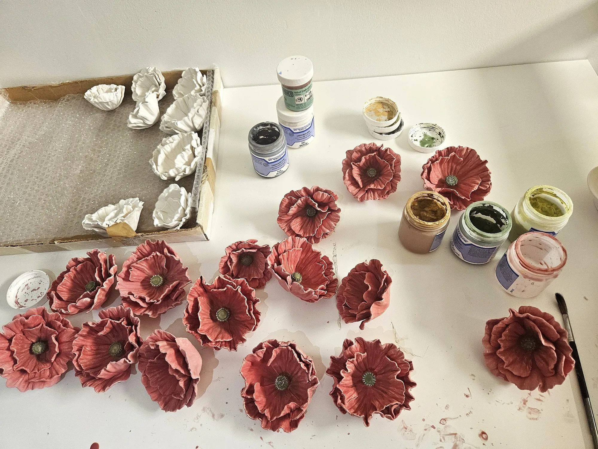Porcelain poppies at various stages of completion in the studio, surrounded by paint jars